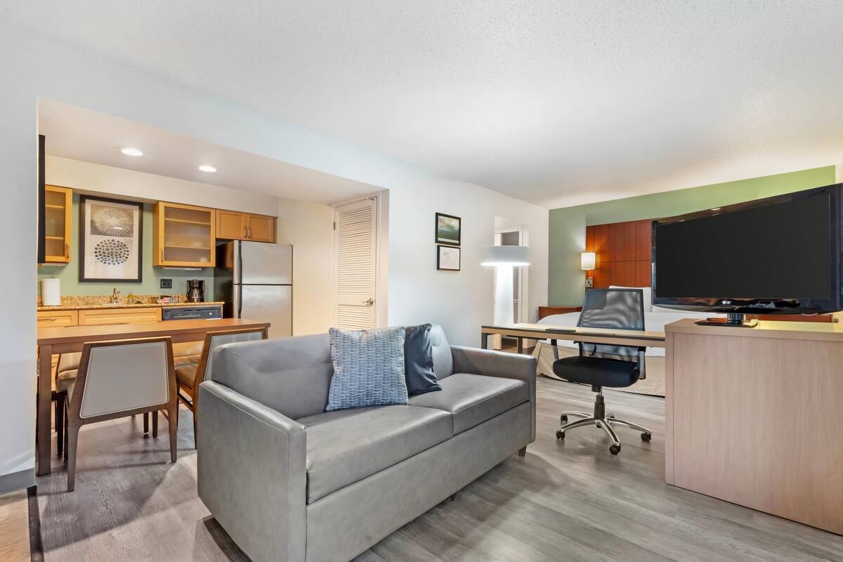 A modern apartment with a kitchenette, a sofa, a desk, and a TV.