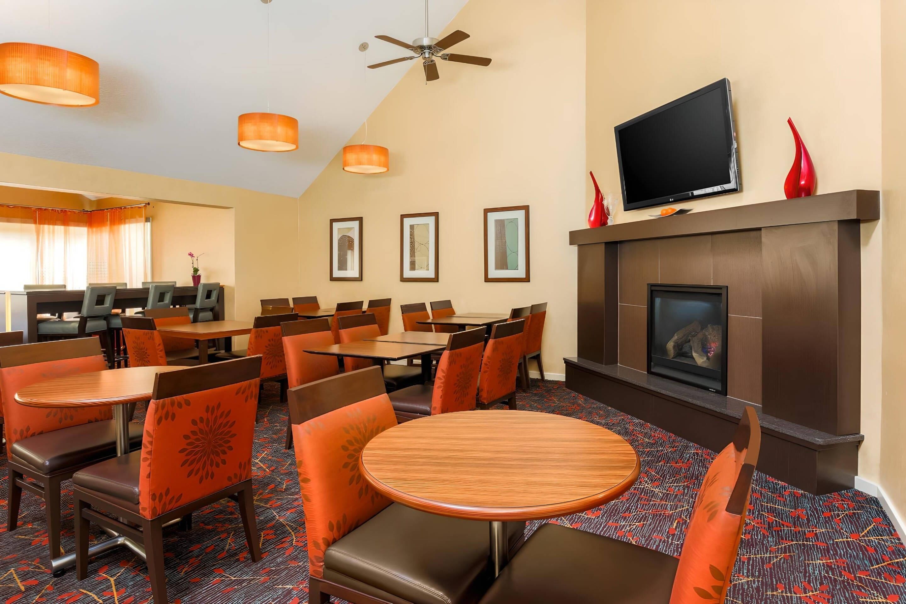 A hotel lobby with multiple dining tables and chairs, a television, and framed artwork on the wall.