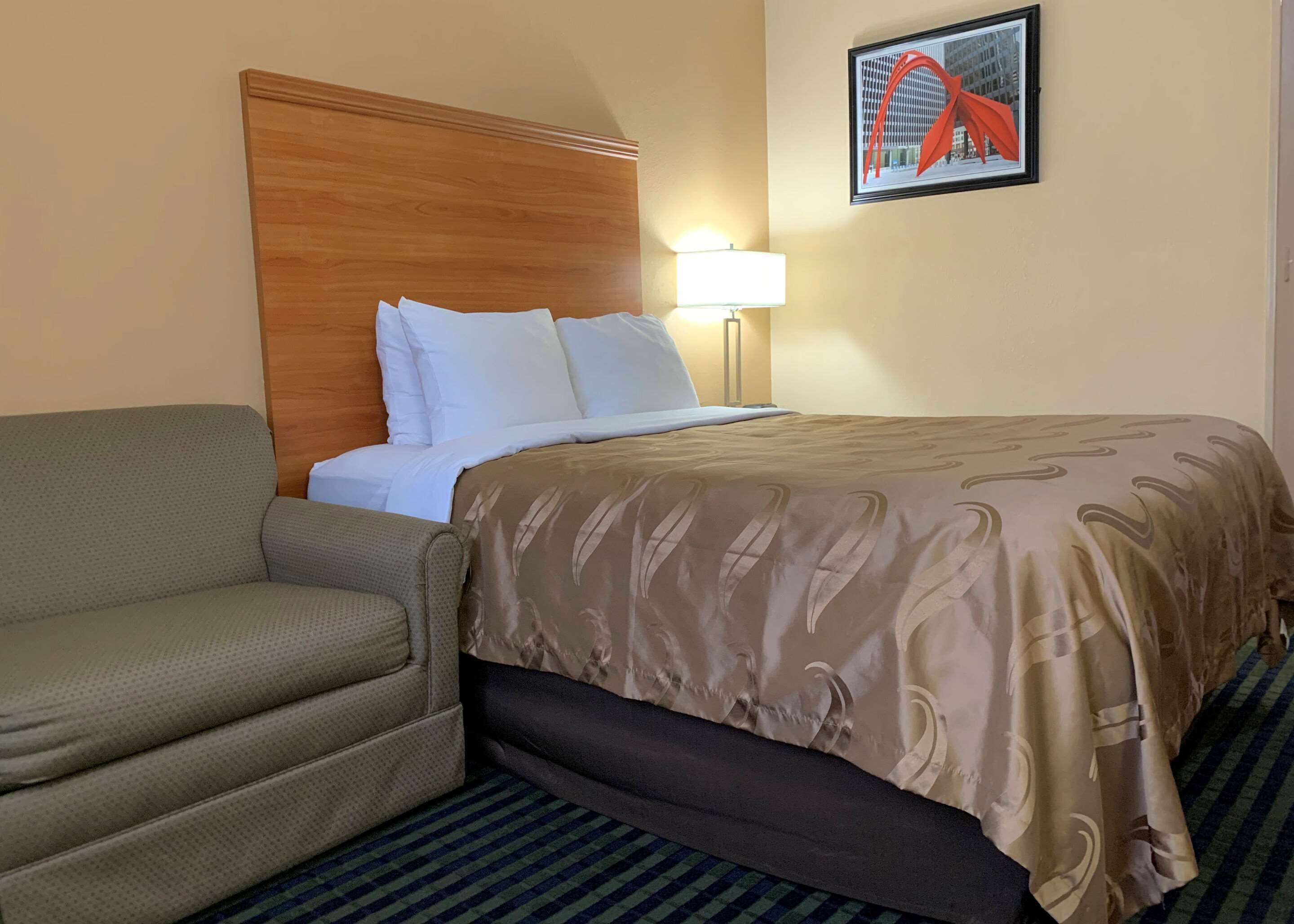 A hotel room with a bed, a sofa, a lamp, and a framed picture on the wall.