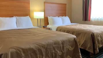 Quarto de hotel com duas camas, cada uma com roupa de cama branca e colcha castanha. Há uma mesa de cabeceira com uma luminária entre as camas.