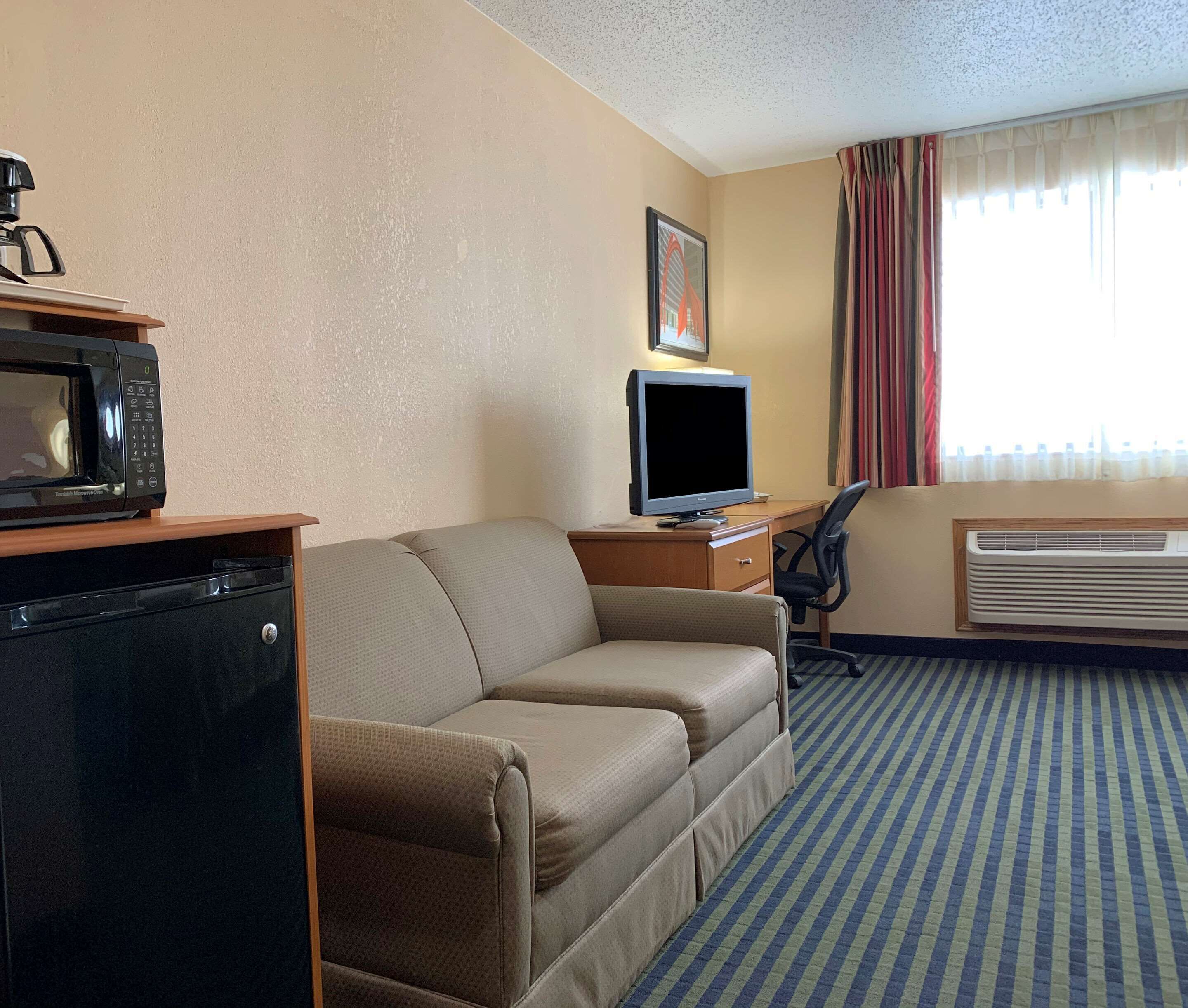 A hotel room with a sofa, a television, a microwave, a small desk, and a window with curtains.