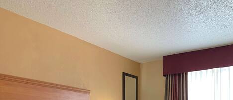 A hotel room with a large bed, a nightstand with a lamp, a mirror, and a window with curtains.