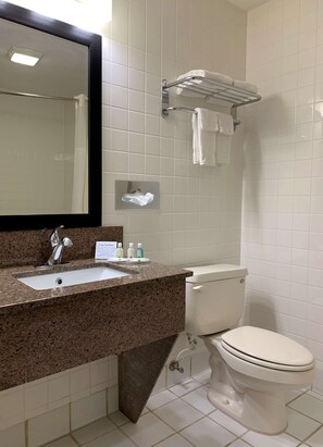 A bathroom with a granite countertop sink, a mirror, a towel rack, a toilet, and a sign with a message.
