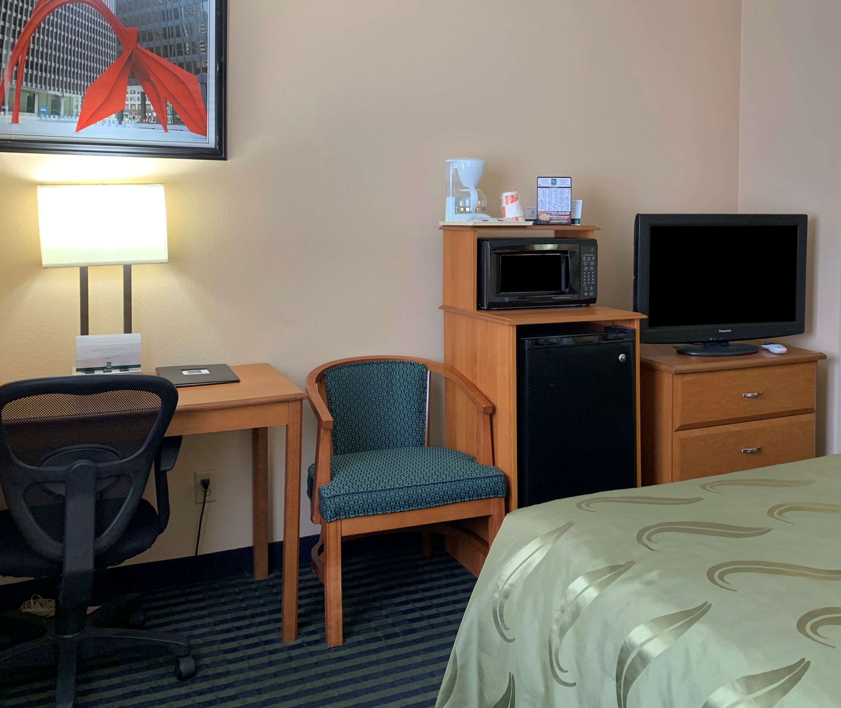 Ein Hotelzimmer mit Schreibtisch, Stuhl, Bett, Fernseher, Mikrowelle und Kühlschrank.
