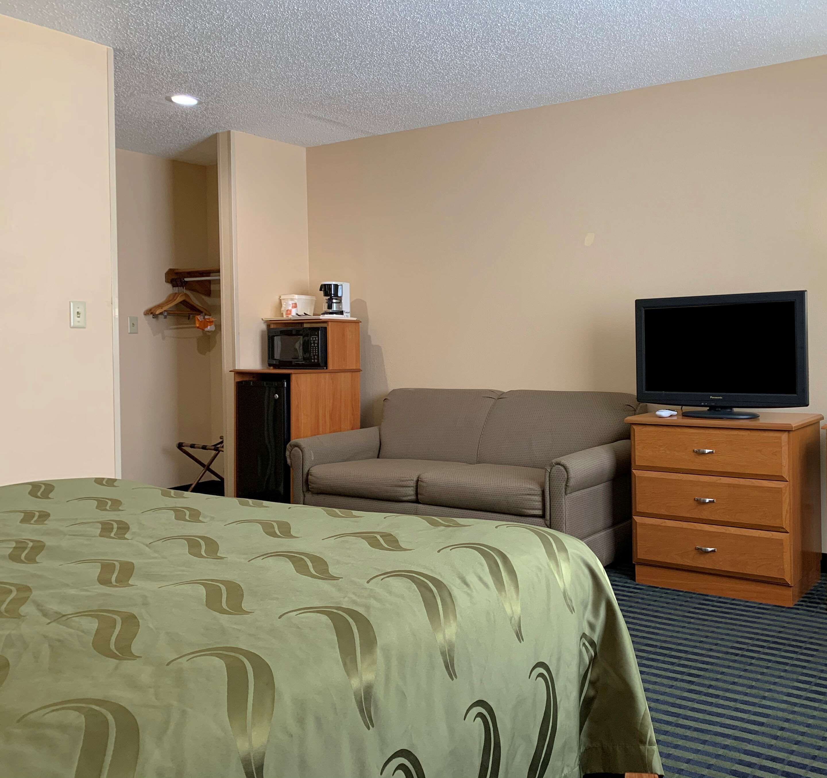 Une chambre d’hôtel équipée d’un lit, d’un canapé, d’une télévision, d’une commode et d’un four à micro-ondes posé sur un meuble.