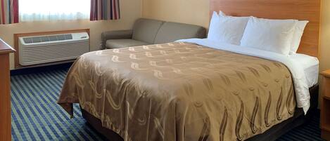 A hotel room with a large bed, a bedside table, a chair, a window with curtains, and a wall-mounted air conditioner.
