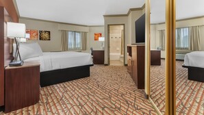 Habitación de hotel con una cama grande, un escritorio, una silla, un espejo y un baño visible a través de una puerta abierta.