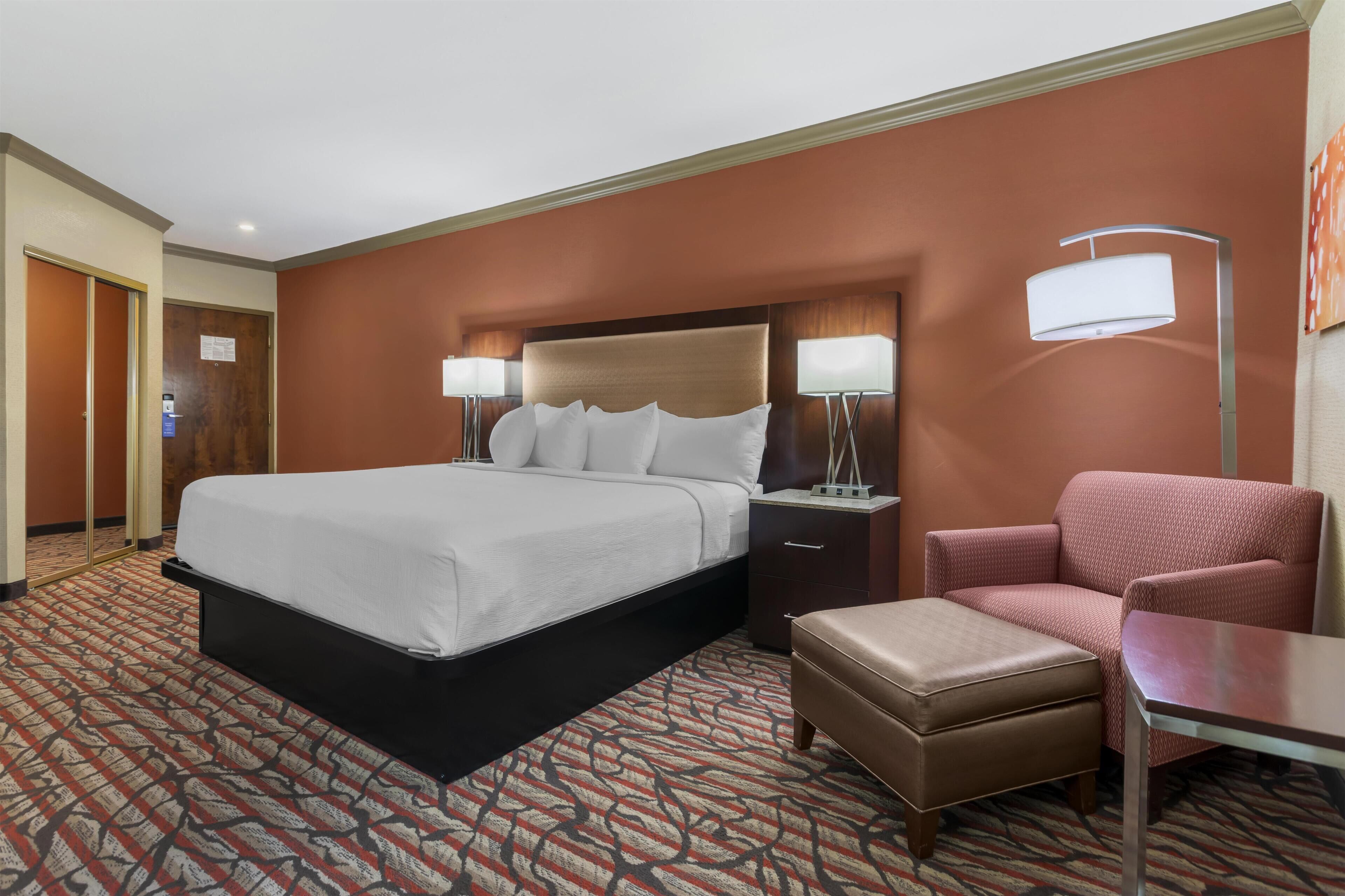 Una habitación de hotel con una cama grande, un escritorio, una silla y dos lámparas de noche.
