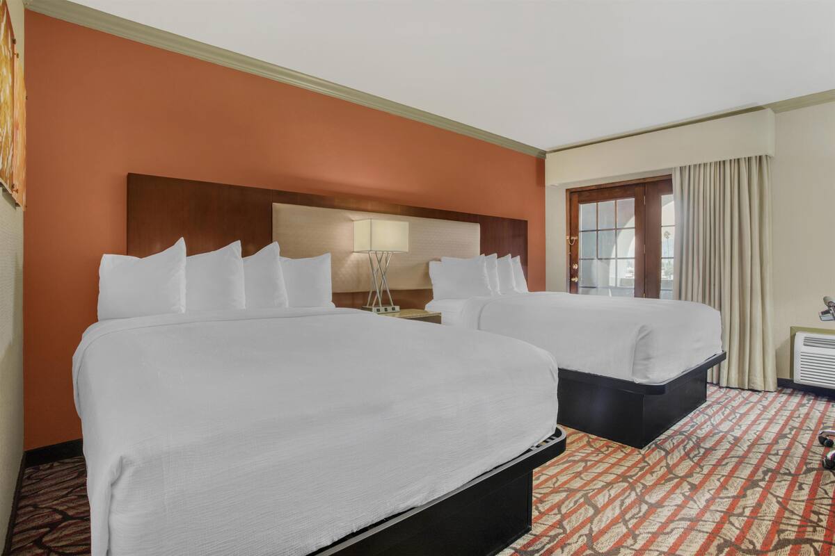 A hotel room with two beds, a headboard, a lamp, a window with curtains, and a patterned carpet.