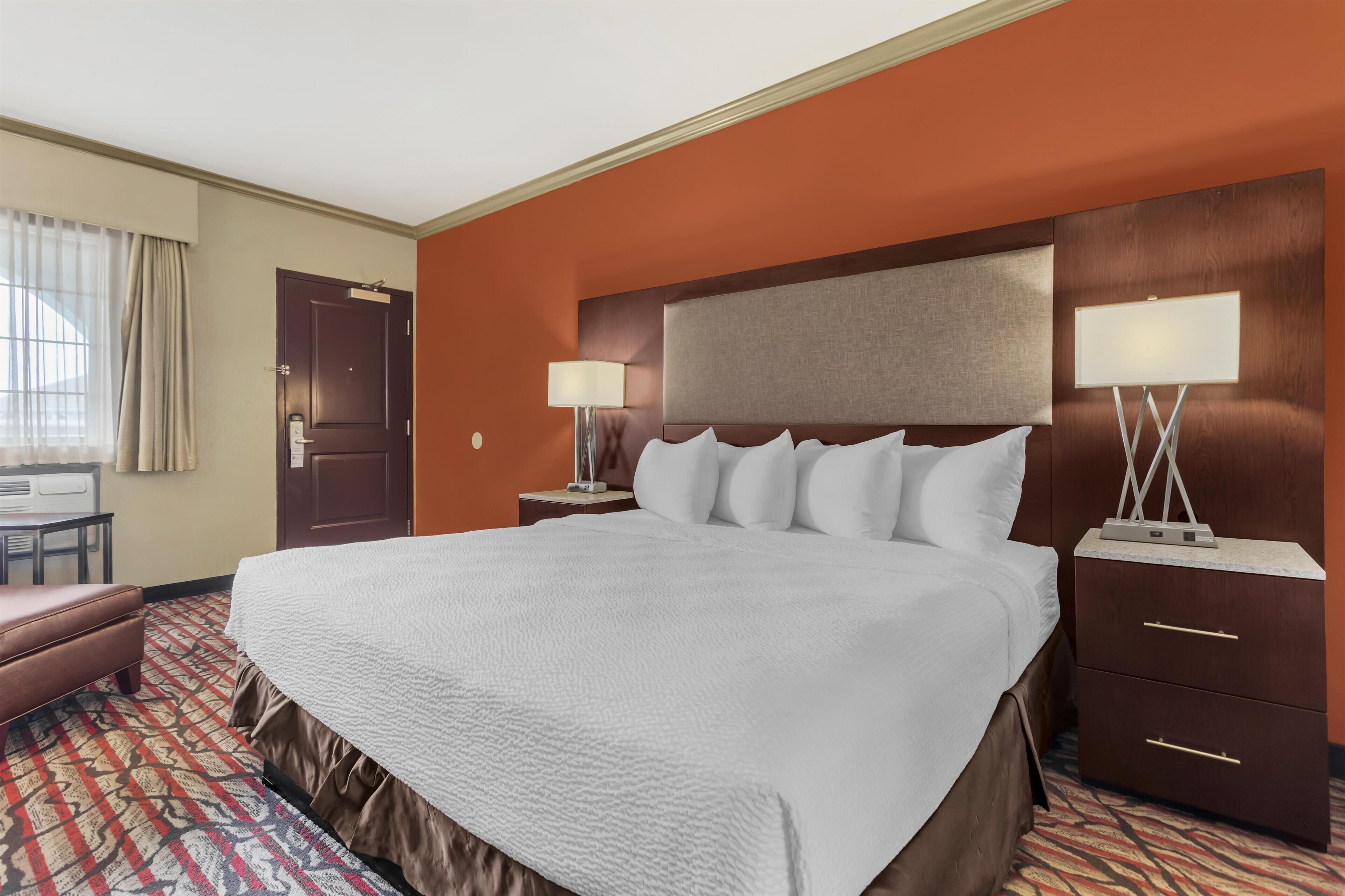 A hotel room with a large bed, two bedside tables with lamps, a desk, and a chair.