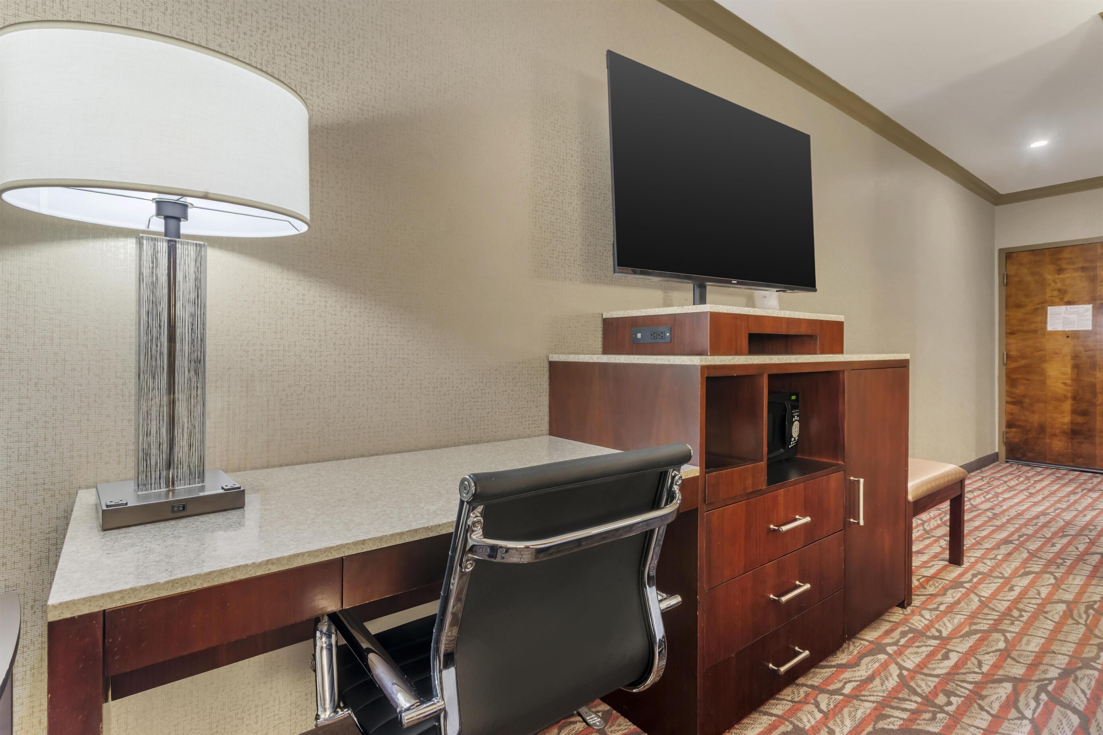 A hotel room with a desk, chair, TV, and a wooden cabinet.