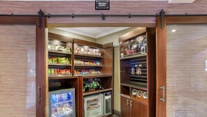 Una despensa bien organizada con estantes llenos de refrigerios, bebidas y un refrigerador.