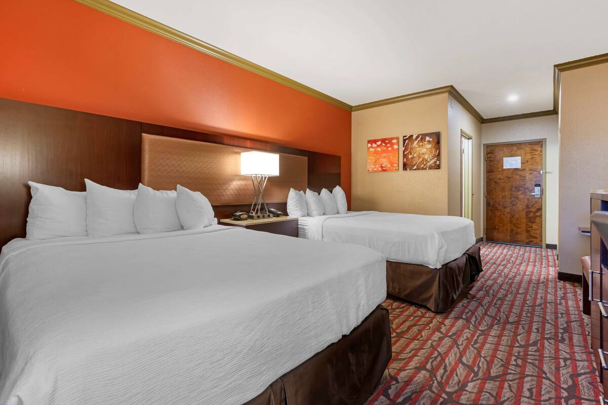 A hotel room with two beds, a nightstand, a lamp, and a door with a sign.