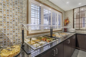 A buffet area with multiple food stations, a patterned wall, and a window with blinds.