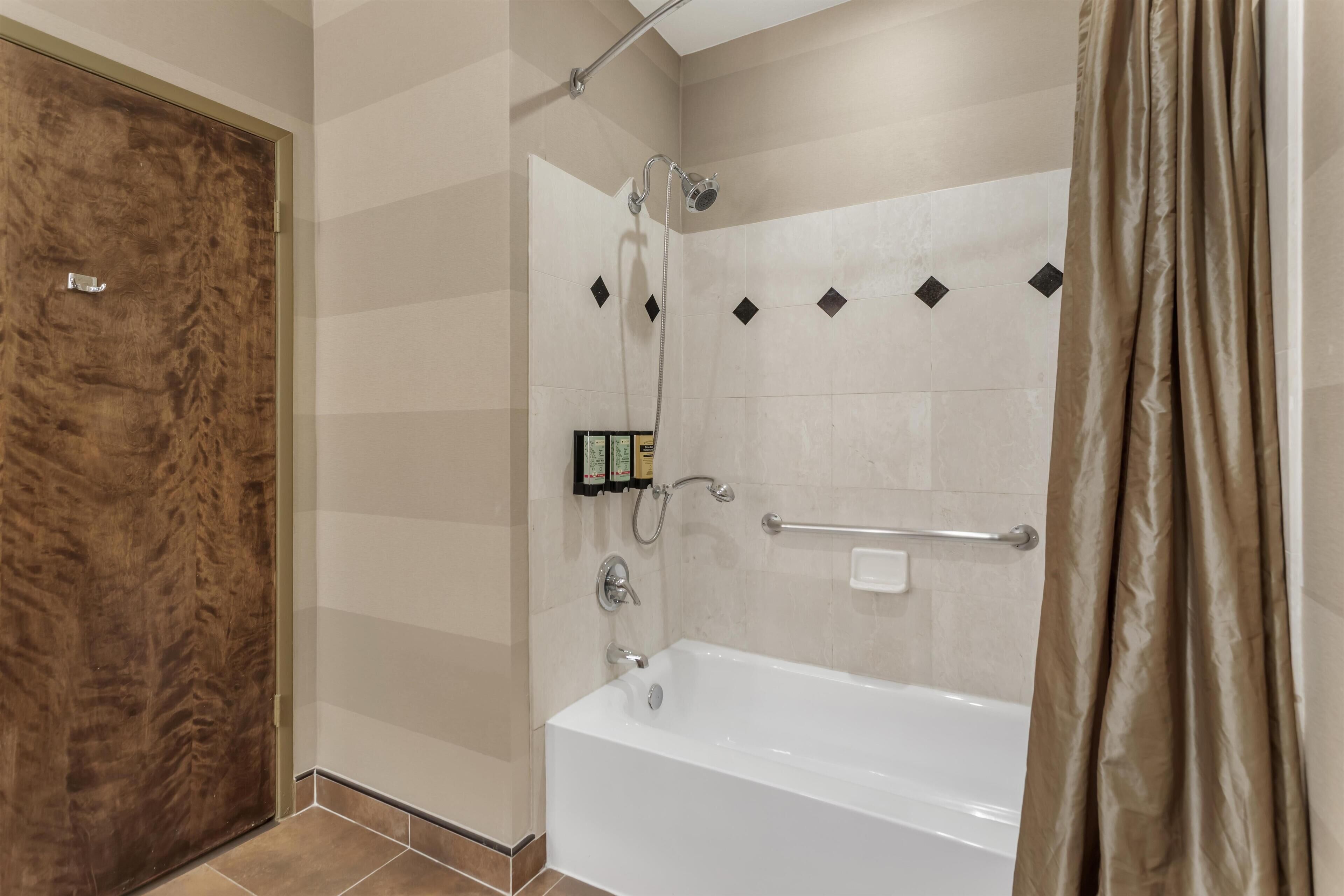 A modern bathroom with a walk-in shower, a bathtub, and a wooden door.