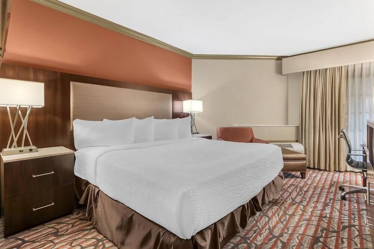 A hotel room with a large bed, a desk, a chair, and a lamp.