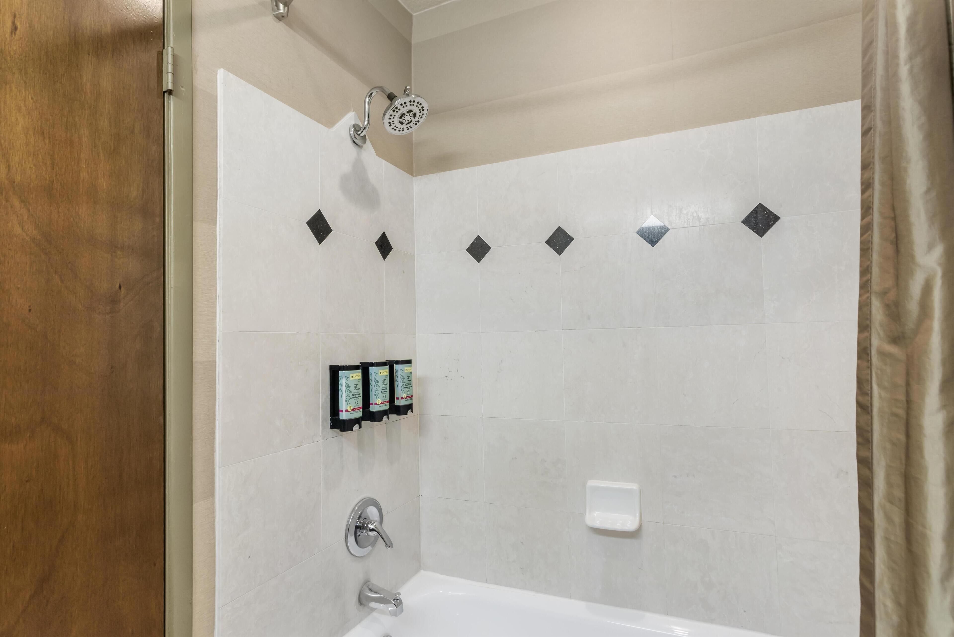A bathroom with a bathtub, a showerhead, and three soap dispensers on the wall.