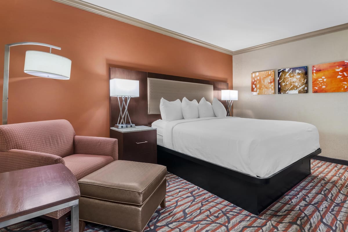 A hotel room with a bed, a desk, a chair, a nightstand, and a lamp.