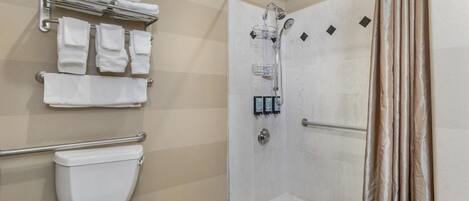 Un baño con inodoro, ducha con puerta de cristal y toallero con toallas dobladas.