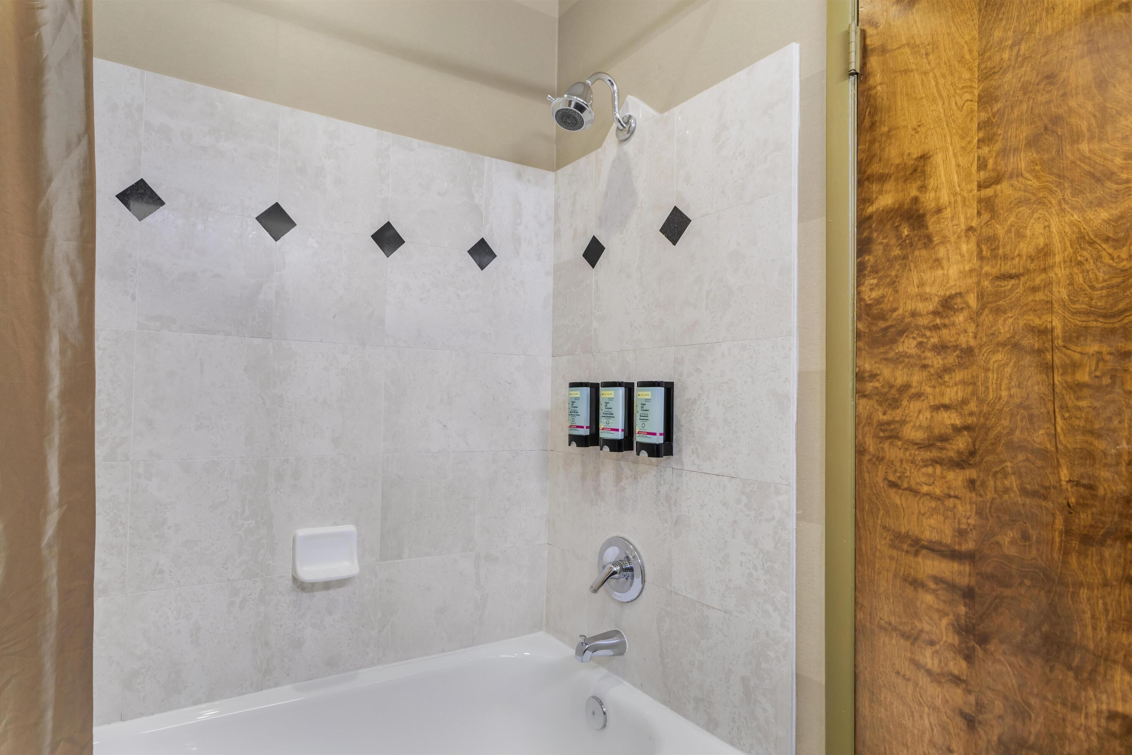 A modern bathroom with a bathtub, a showerhead, and a soap dispenser.