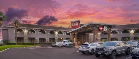 Un hotel con entrada cubierta, varios espacios de estacionamiento y un cielo al atardecer.