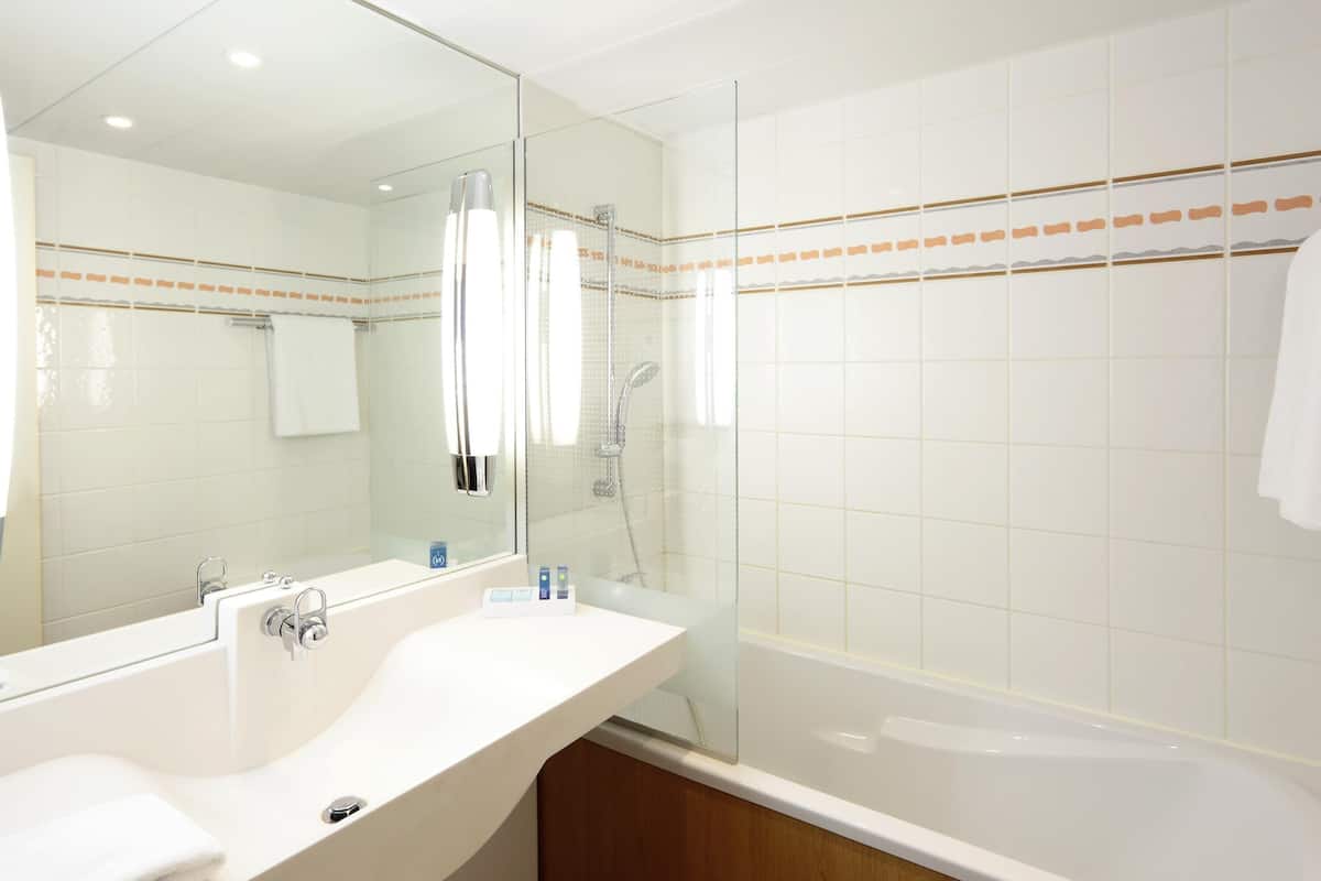A modern bathroom with a large mirror, a bathtub, and a sink.