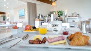 A breakfast table with croissants, sausages, cheese, and a fruit plate.