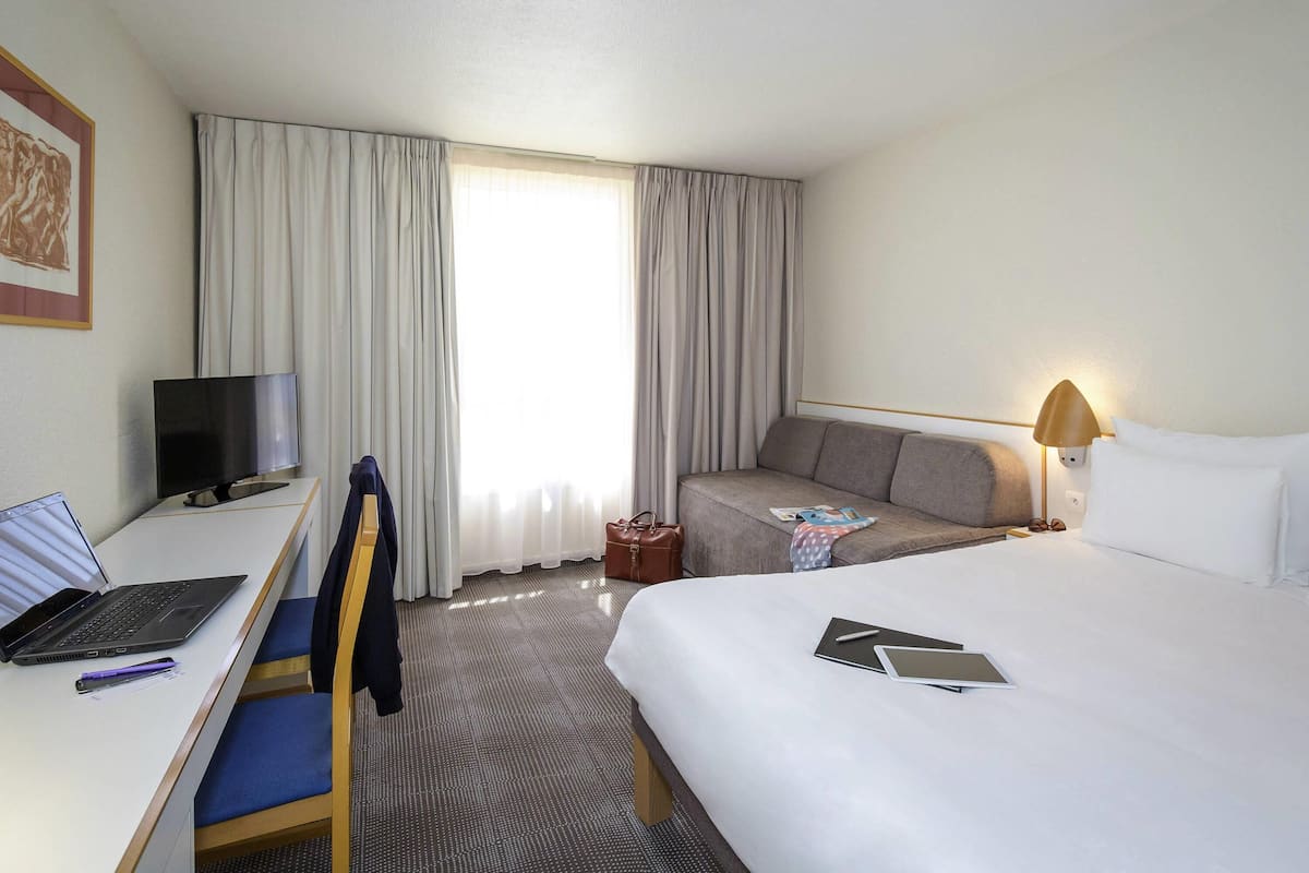 A hotel room with a bed, a desk with a laptop, a TV, and a sofa.