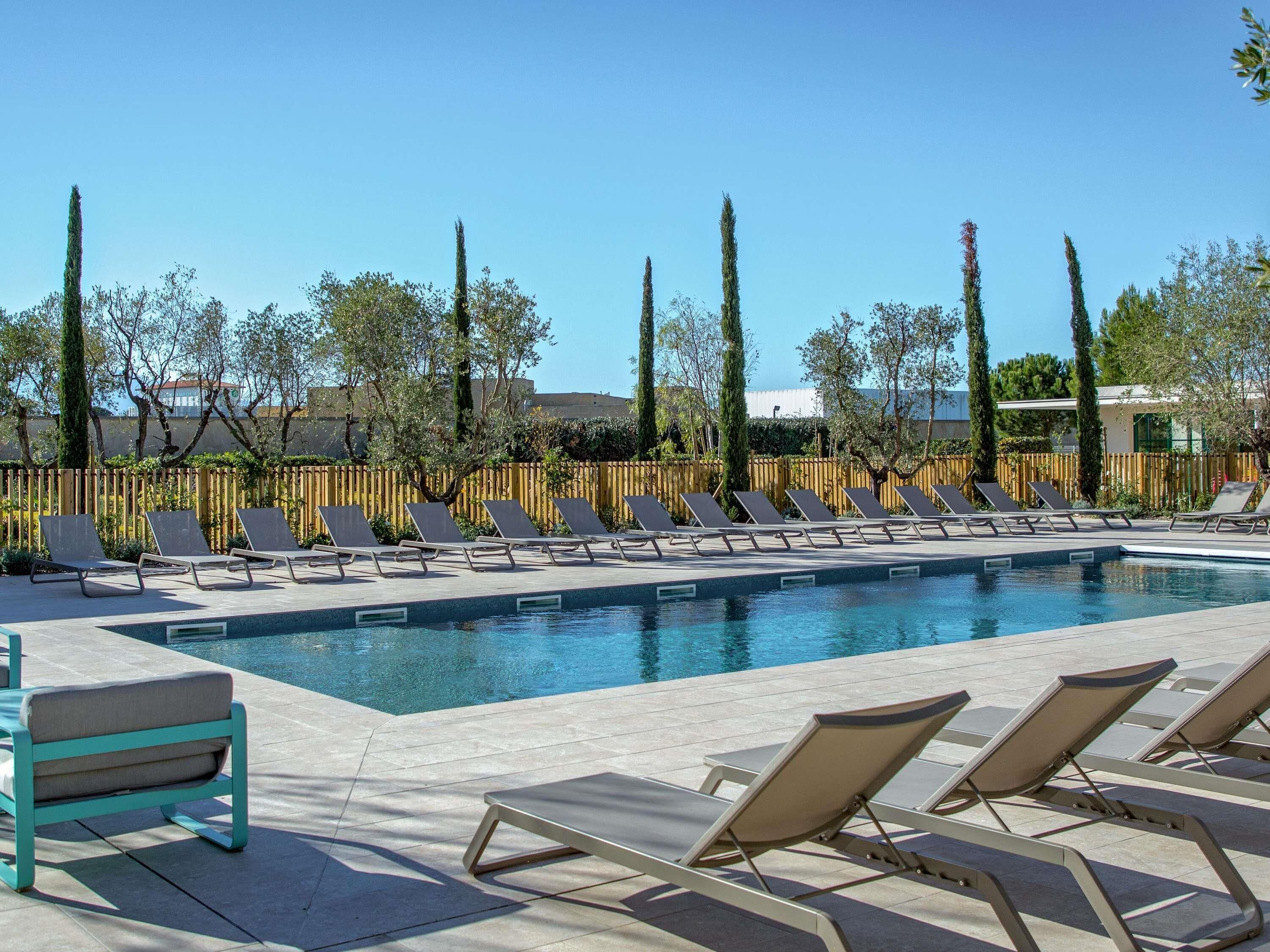 A swimming pool with lounge chairs and a wooden fence in the background.