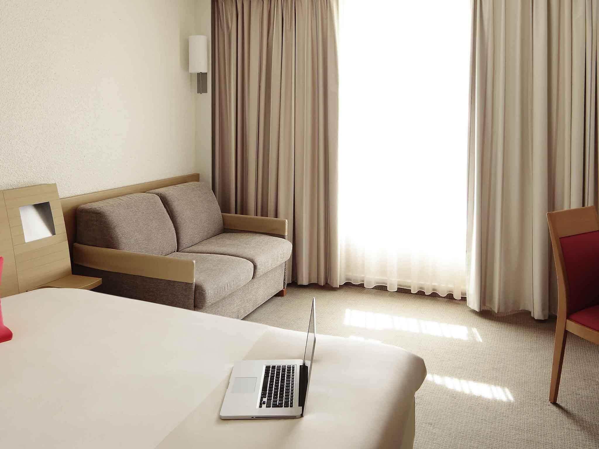 Une chambre d’hôtel avec un lit, un canapé, un ordinateur portable et des rideaux.