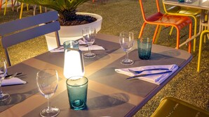 An outdoor dining area with tables set for two, featuring clear glassware and napkins.