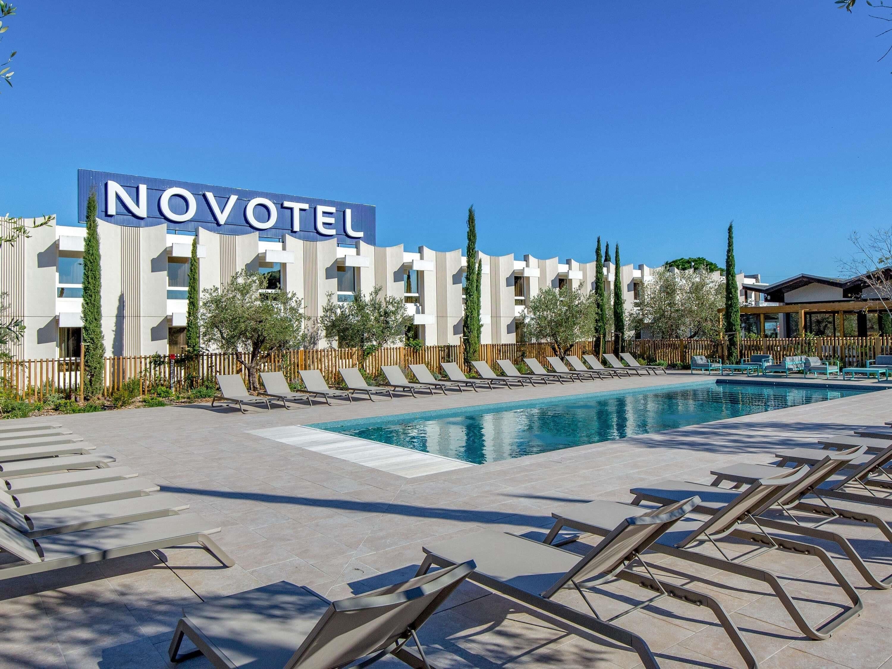Et Novotel hotel med swimmingpool, liggestole og en moderne bygning.
