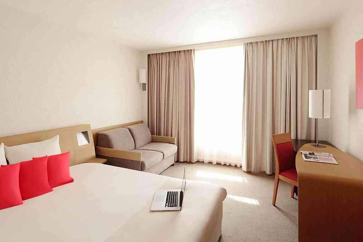 A hotel room with a bed, a desk, a chair, and a window with curtains.