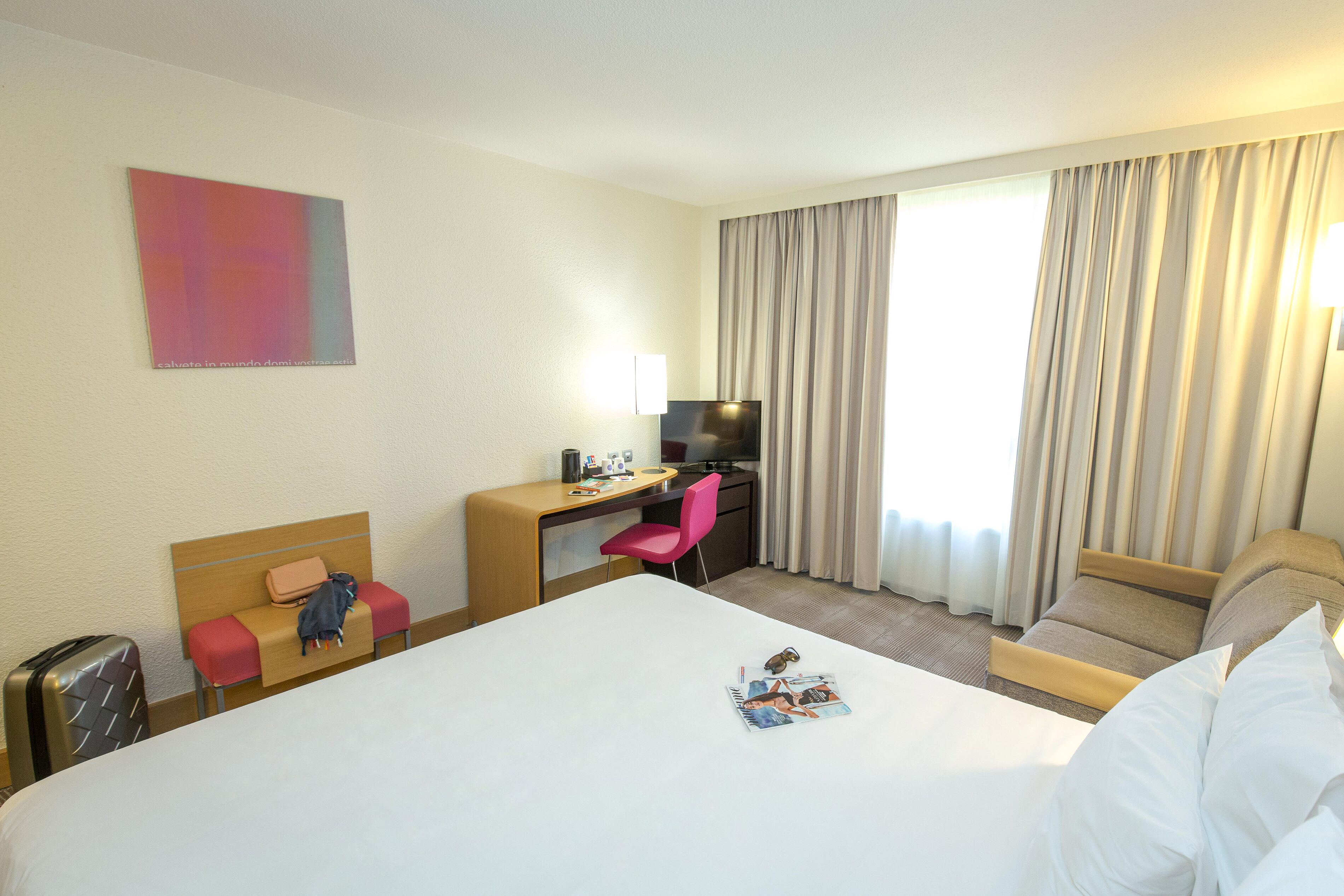 Habitación de hotel con una cama grande, un escritorio con silla, un televisor y una ventana con cortinas.