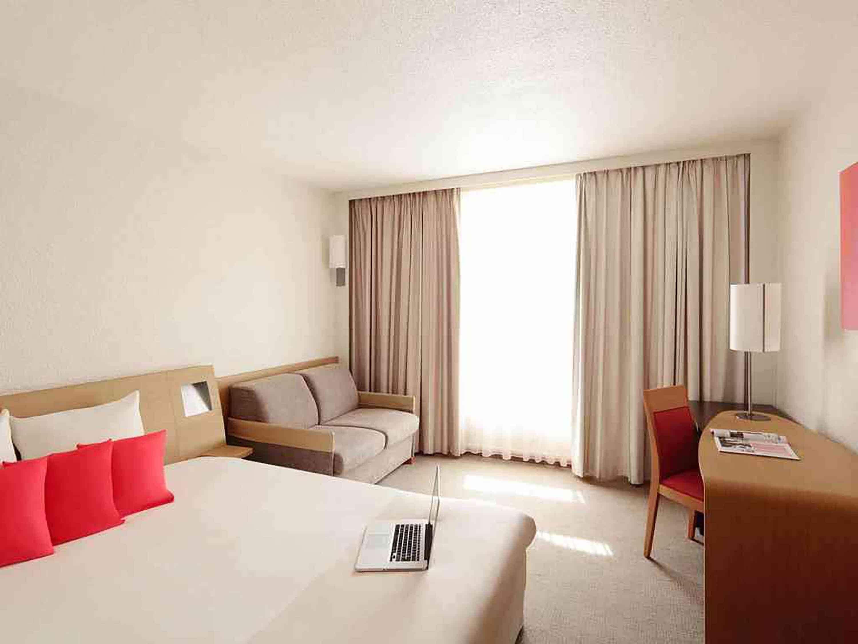 Una habitación de hotel con cama, escritorio, silla y ventana con cortinas.