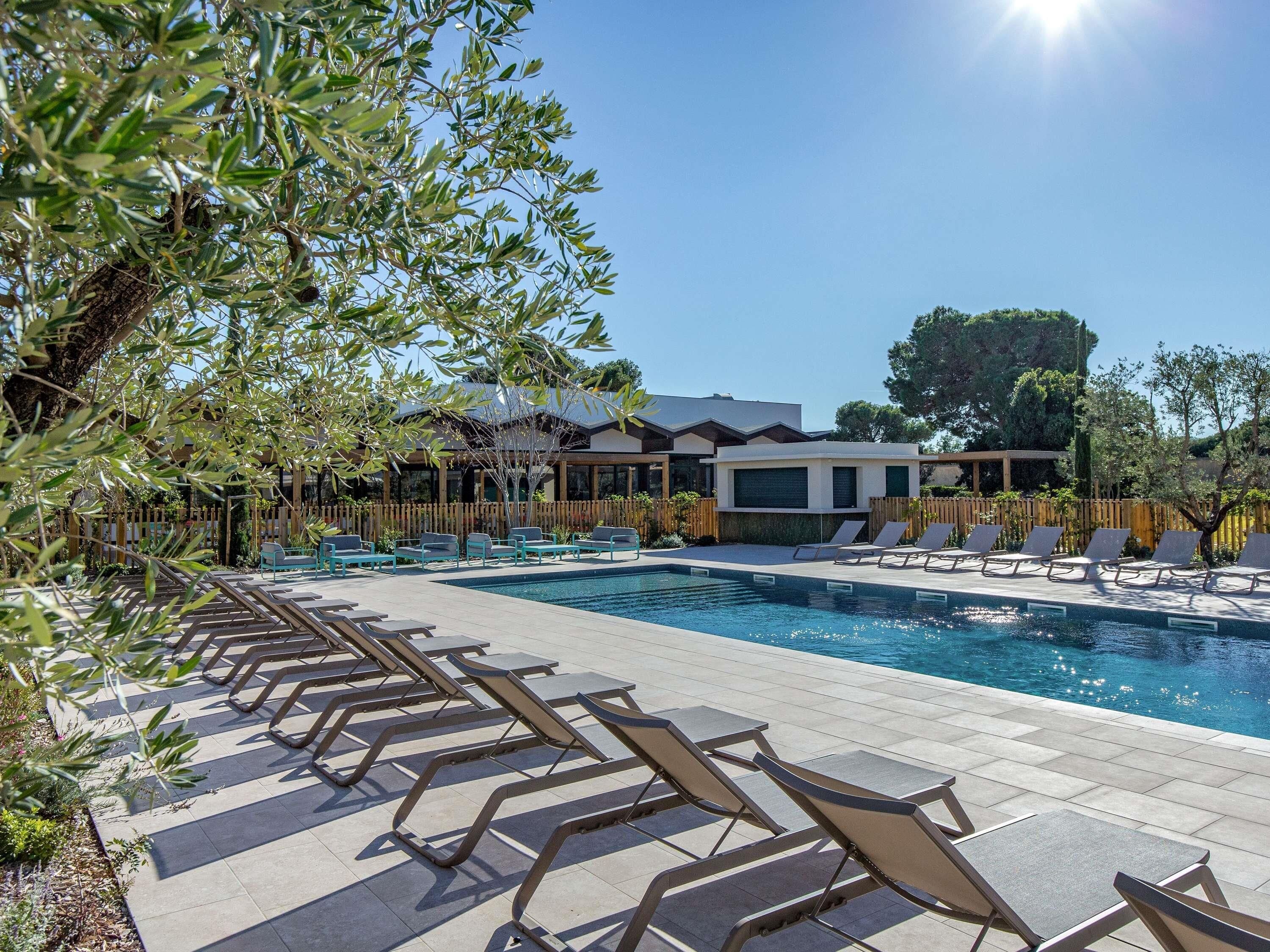 Zona de piscina con sillones de descanso, un edificio moderno y una valla de madera.