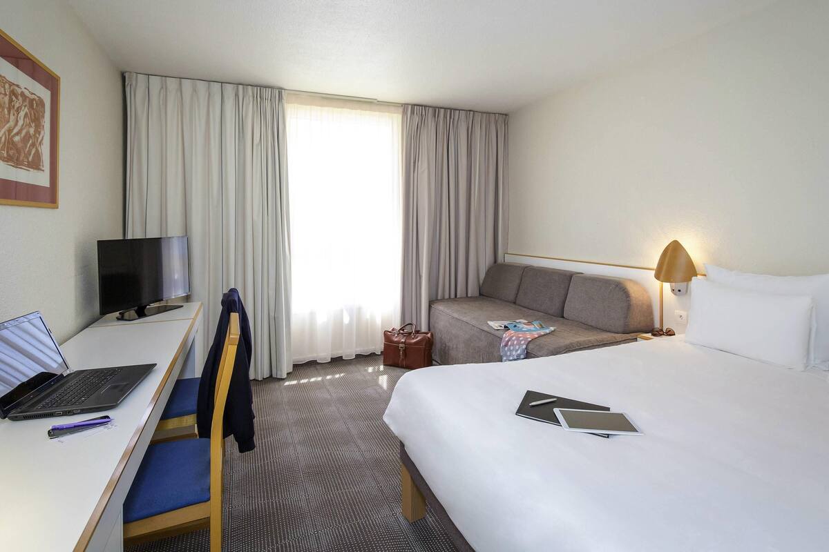 A hotel room with a bed, a desk with a laptop, a TV, and a sofa.