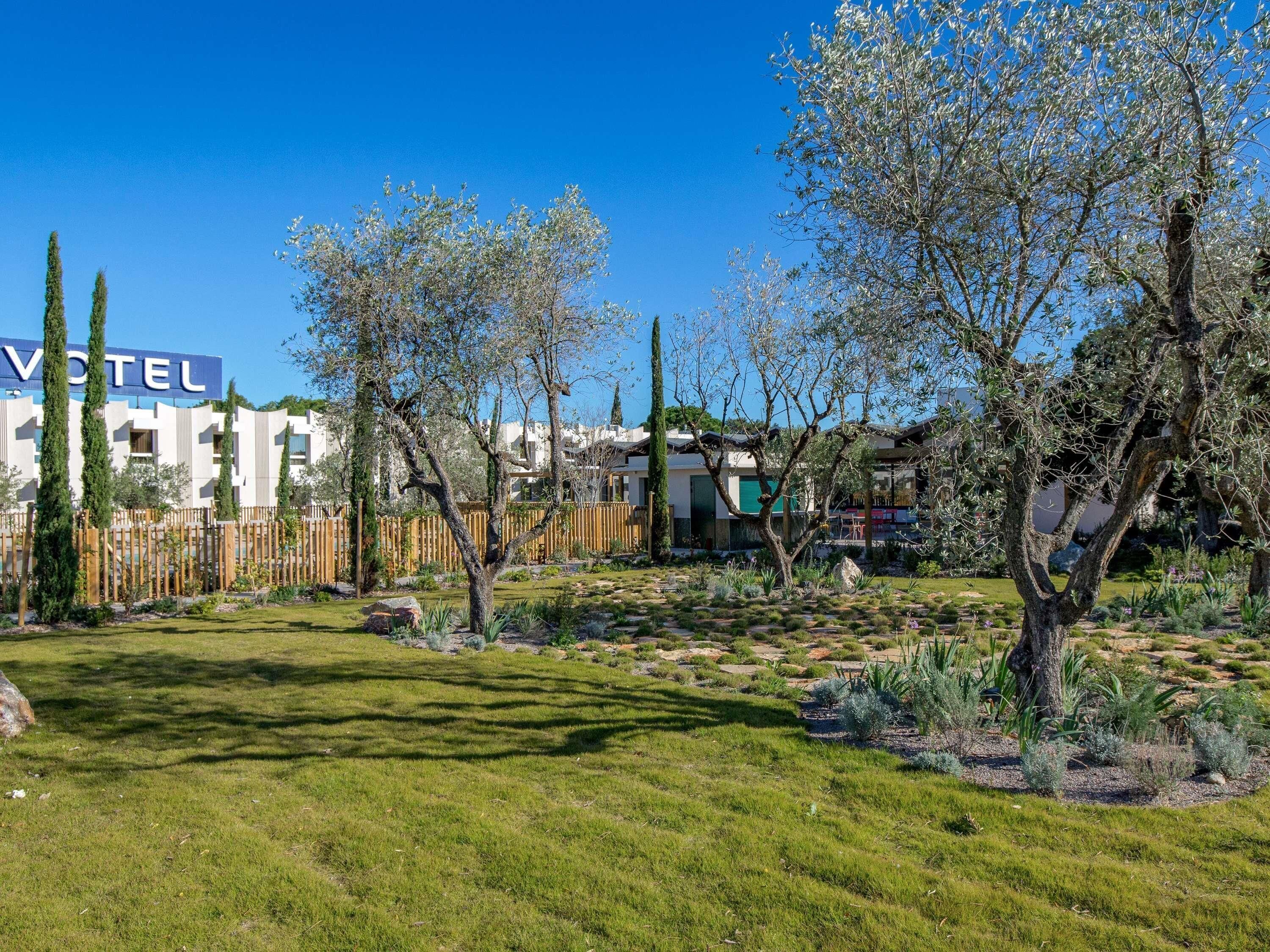 Hotel com placa, jardim cercado e diversas árvores.