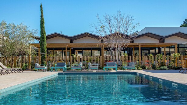 A pool area with lounge chairs and a wooden fence.