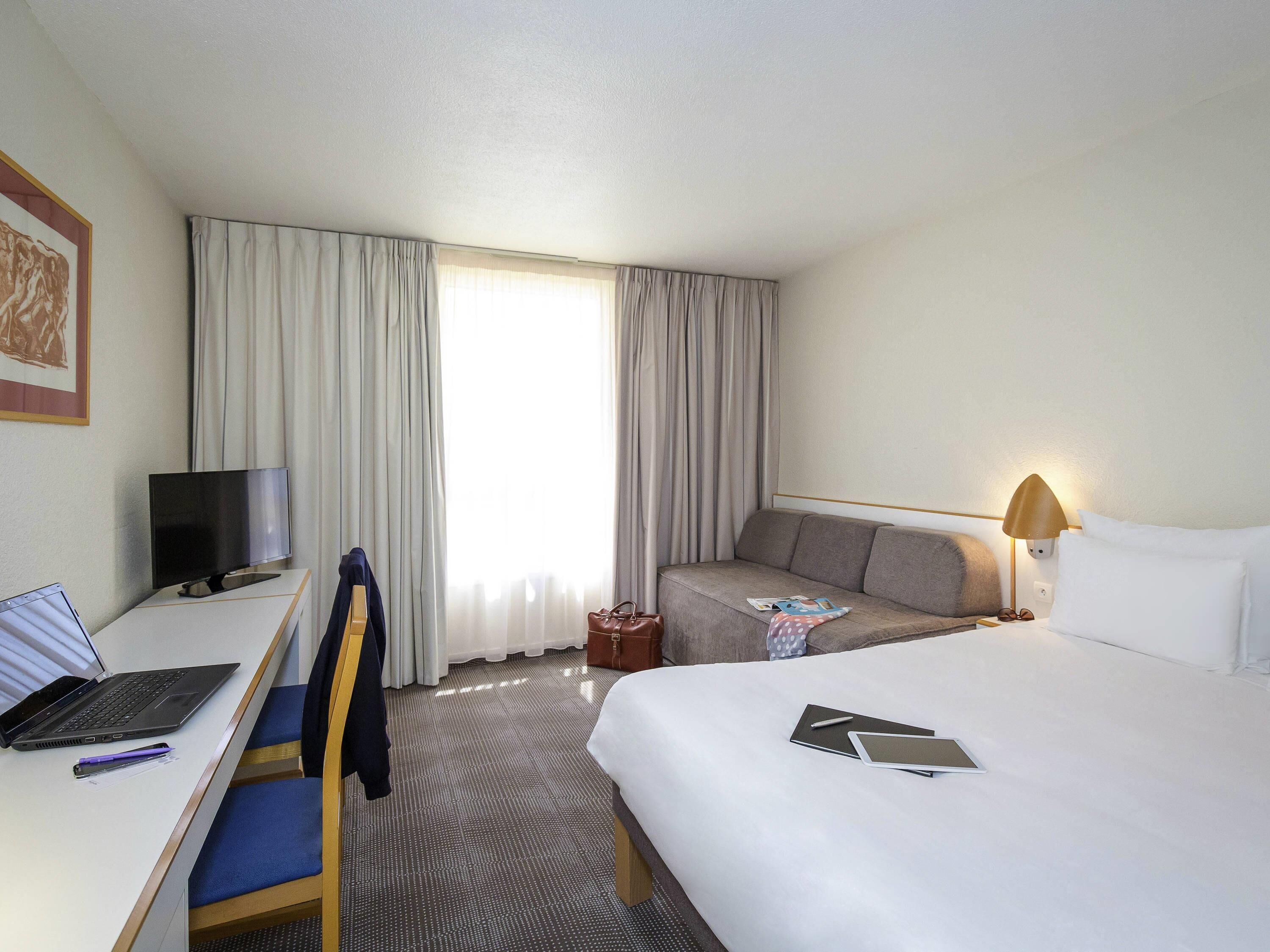 Una habitación de hotel con una cama, un escritorio con una computadora portátil, un televisor y un sofá.