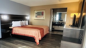 A hotel room with a bed, bedside table, and a mirror. There is a door leading to a bathroom. - Residential Suites Blue Springs by Hotel O I 70 (Grain Valley)