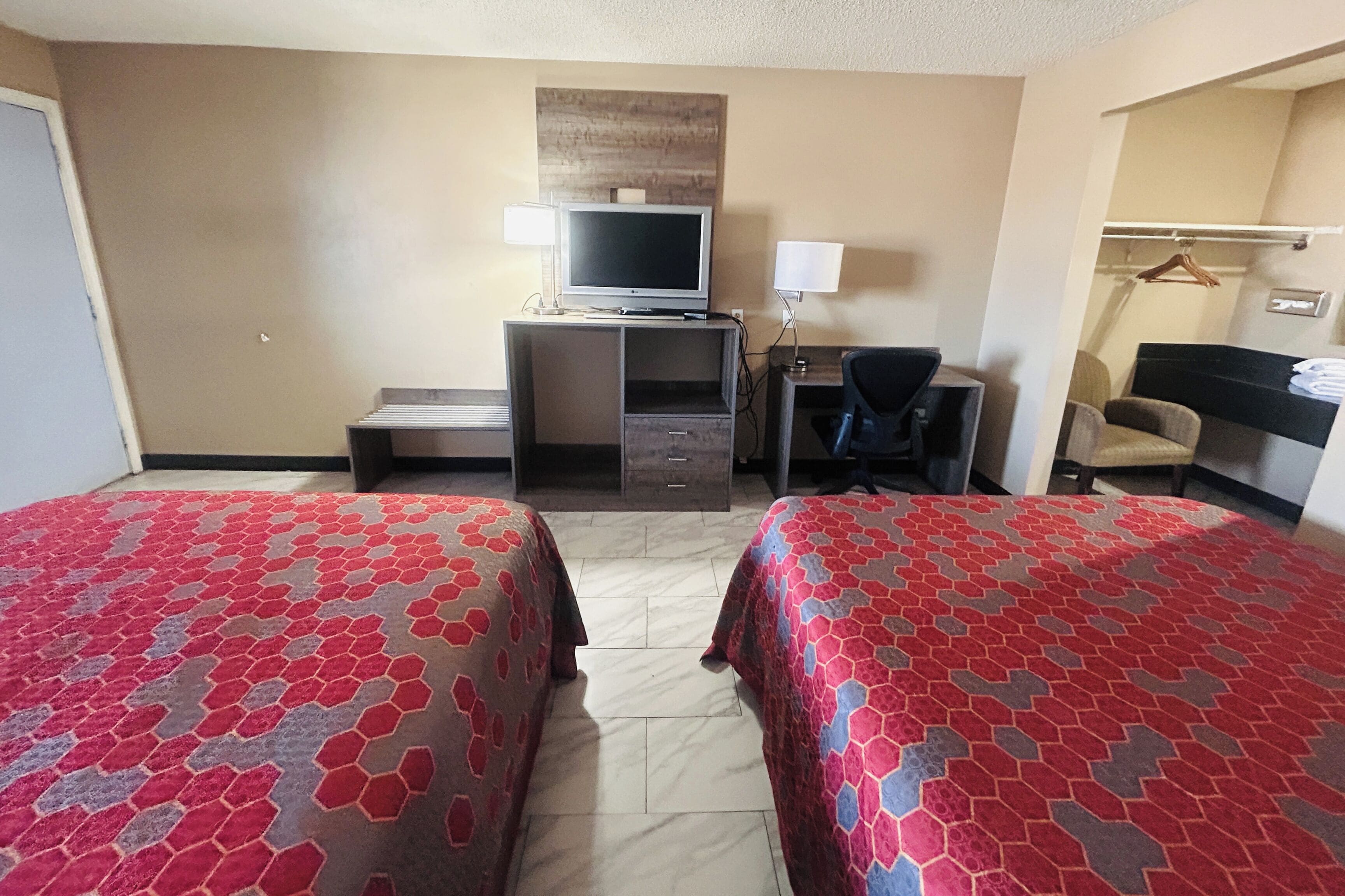 Une chambre d’hôtel avec deux lits, un bureau avec un ordinateur, une télévision et une chaise.