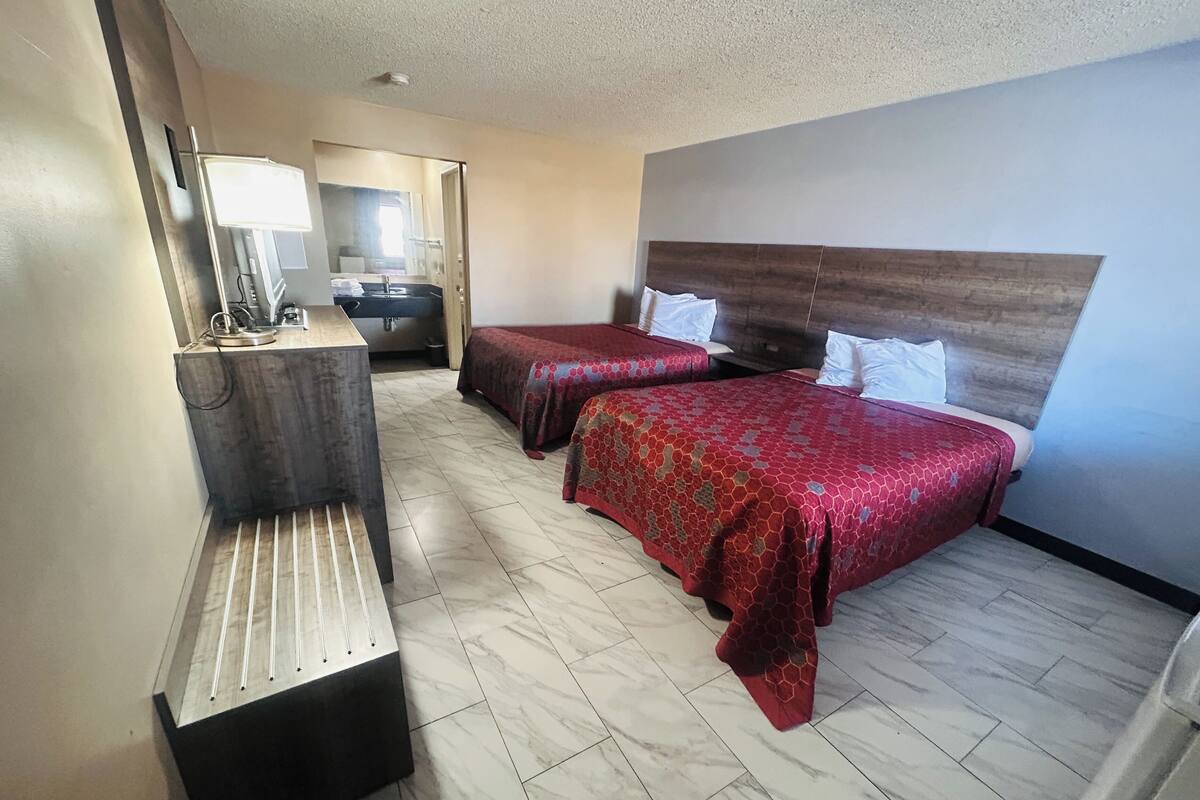 A hotel room with two beds, a desk with a mirror, and a bathroom visible through an open door.