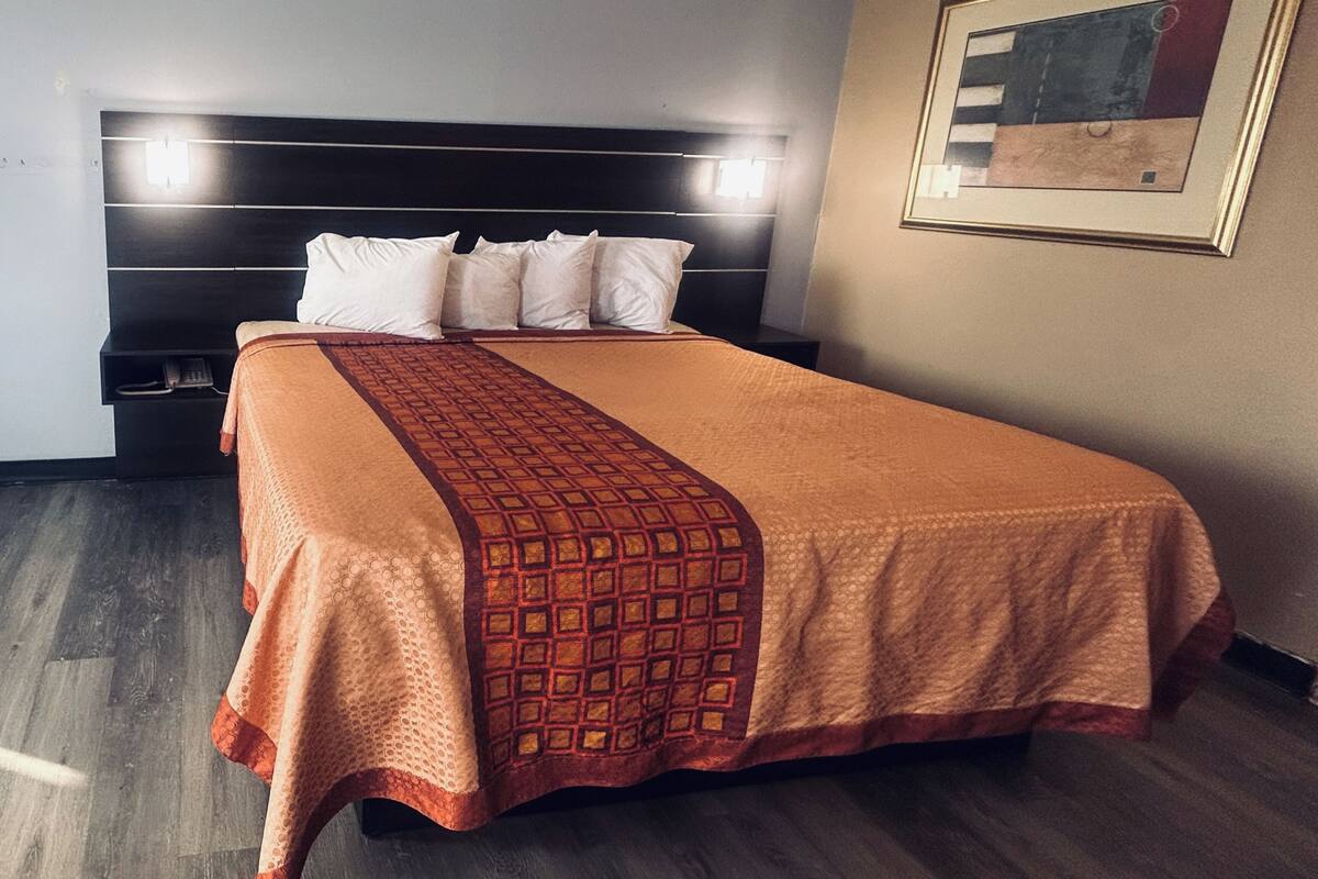 A hotel room with a large bed, a headboard with integrated lighting, a telephone on the nightstand, and a framed picture on the wall.