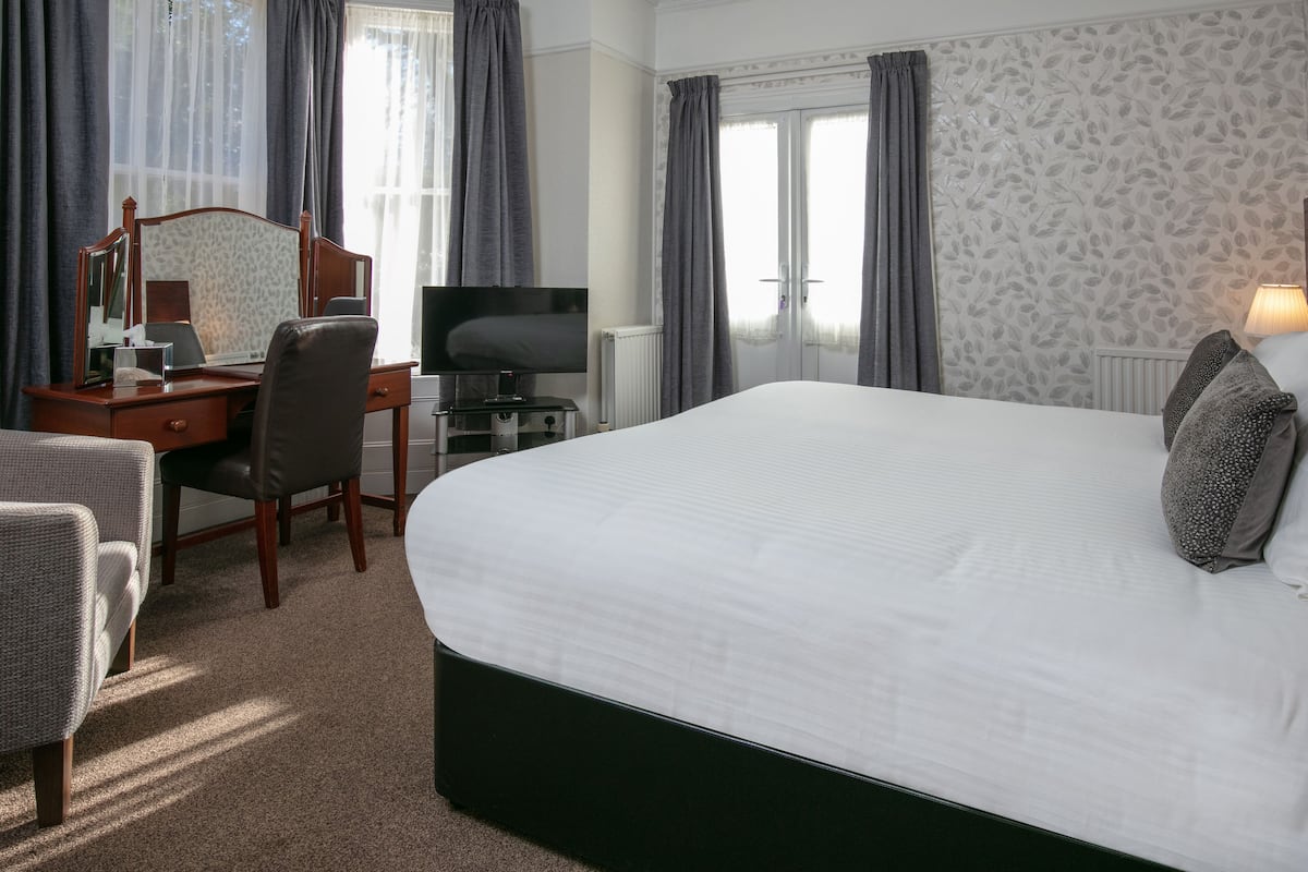 A hotel room with a large bed, a desk with a computer, a television, and a chair.