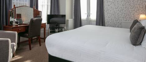 A hotel room with a large bed, a desk with a computer, a television, and a chair.