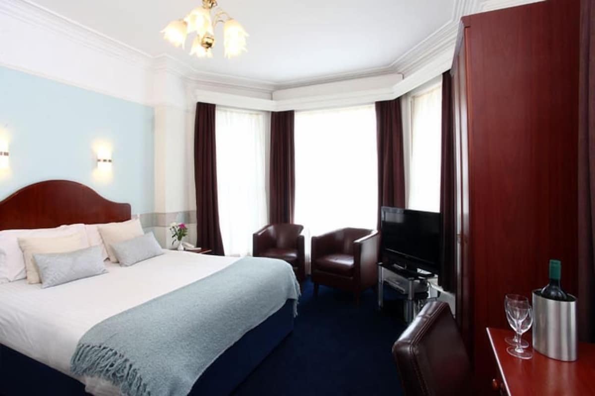 A hotel room with a large bed, a TV, a desk with a computer, and a minibar.
