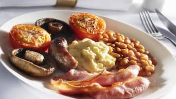 A plate with sausages, mushrooms, baked tomatoes, beans, mashed potatoes, and bacon.