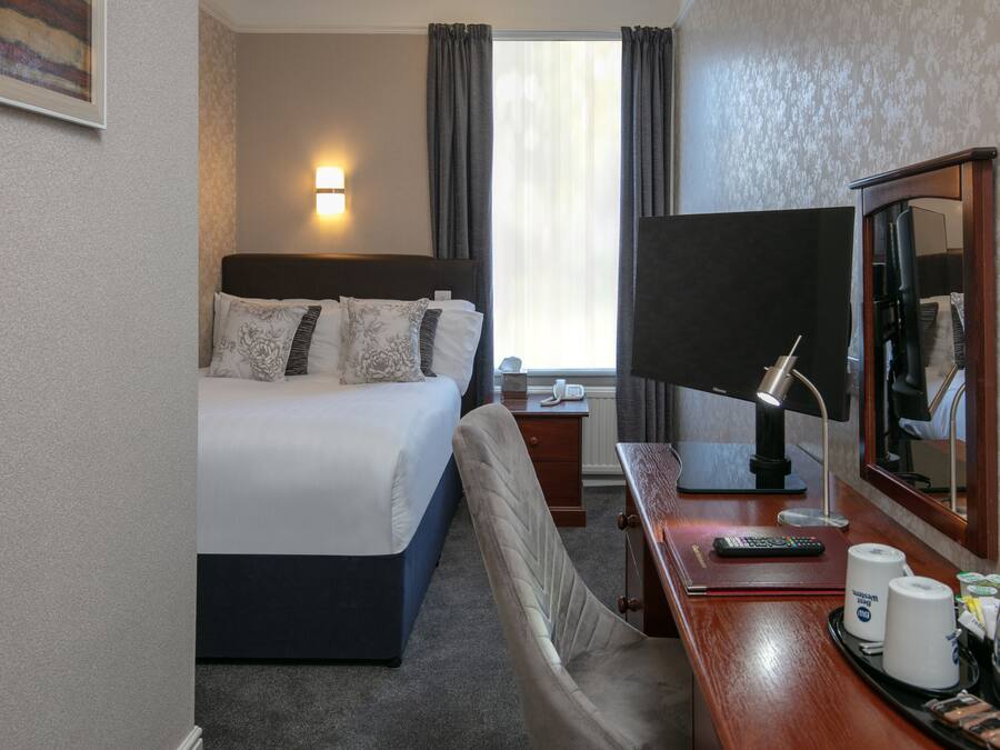 A hotel room with a bed, bedside table, lamp, mirror, and a view of the outside.