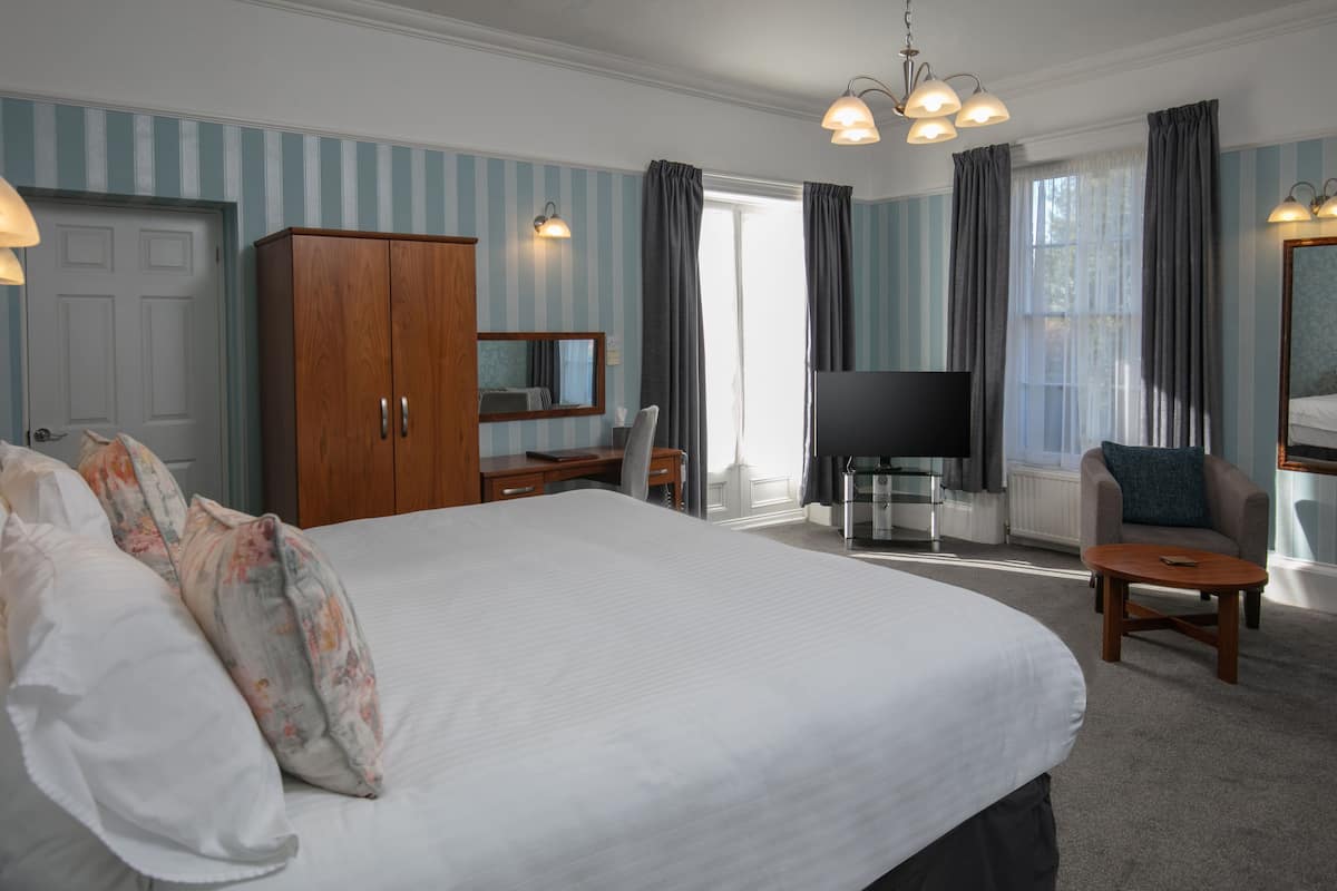 A hotel room with a large bed, a desk, a TV, and a chair.